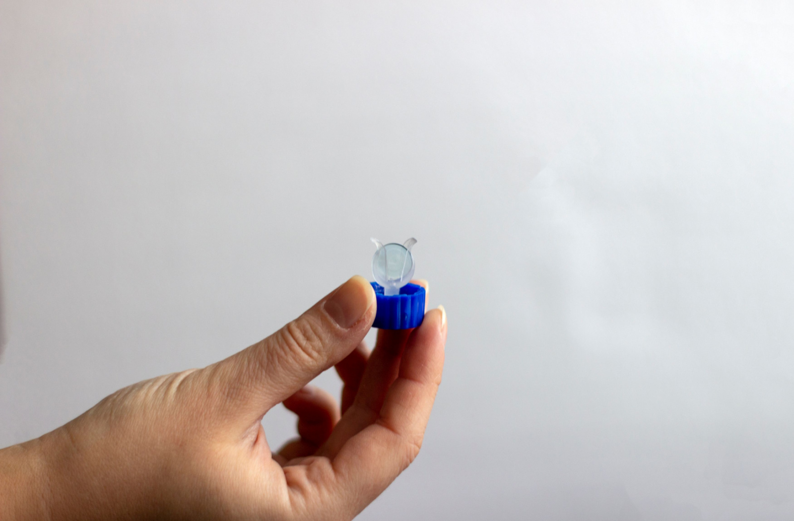 A hand holding an Orthokeratology lens within a container holder.