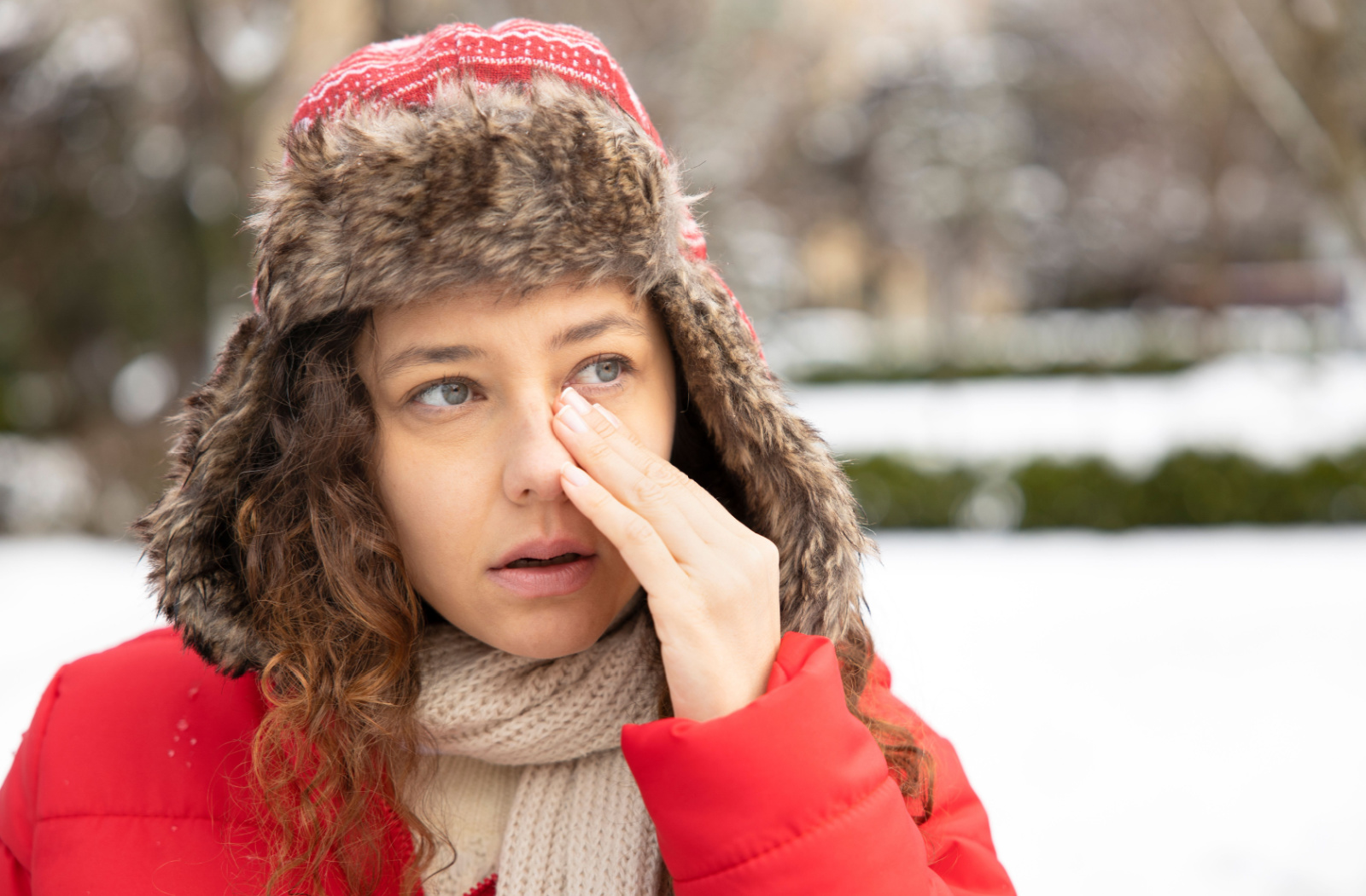 A young woman in a winter coat rubbing her left eye with her left hand.