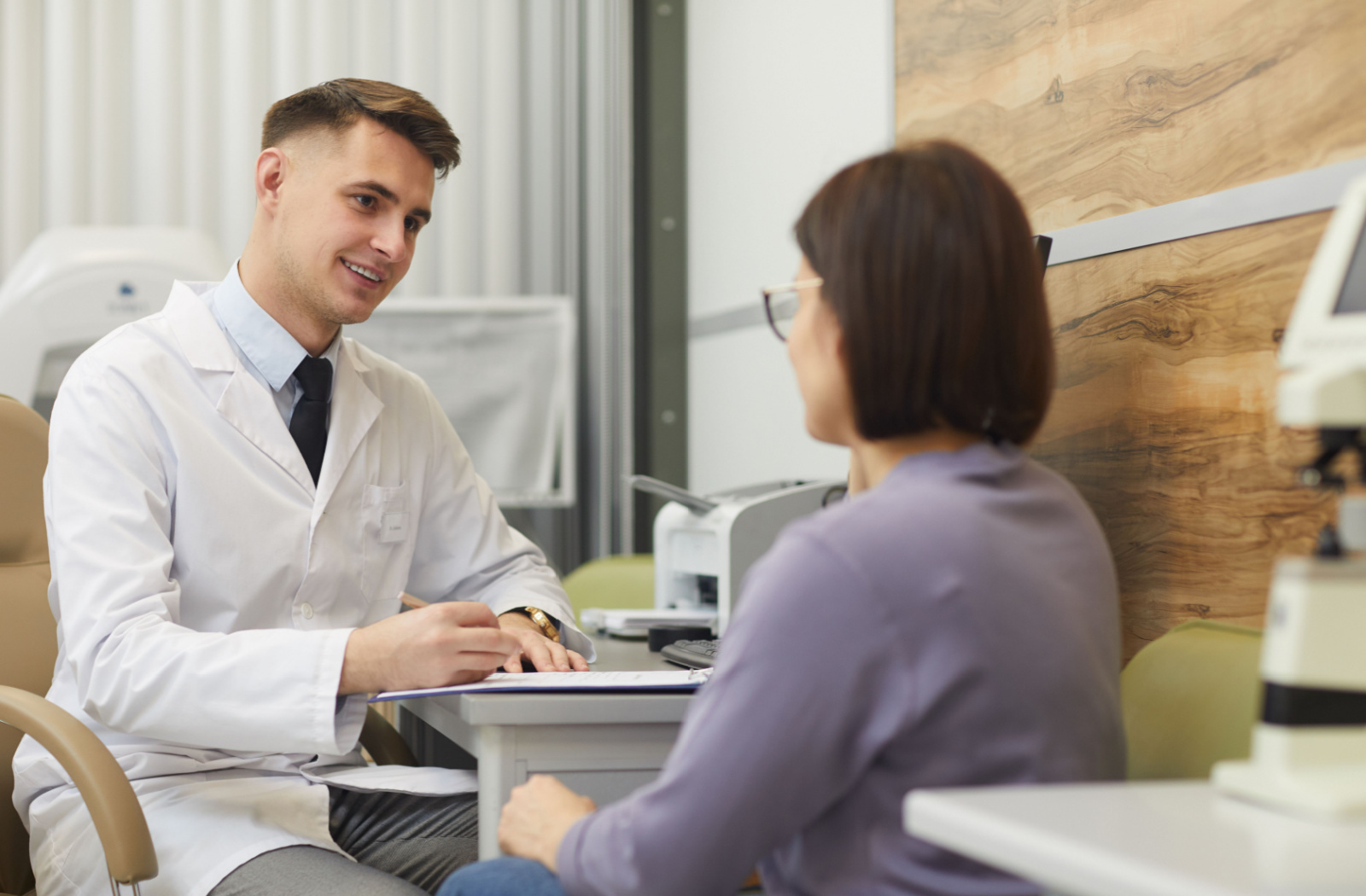A young optometrist taking notes while he listens to his patient.