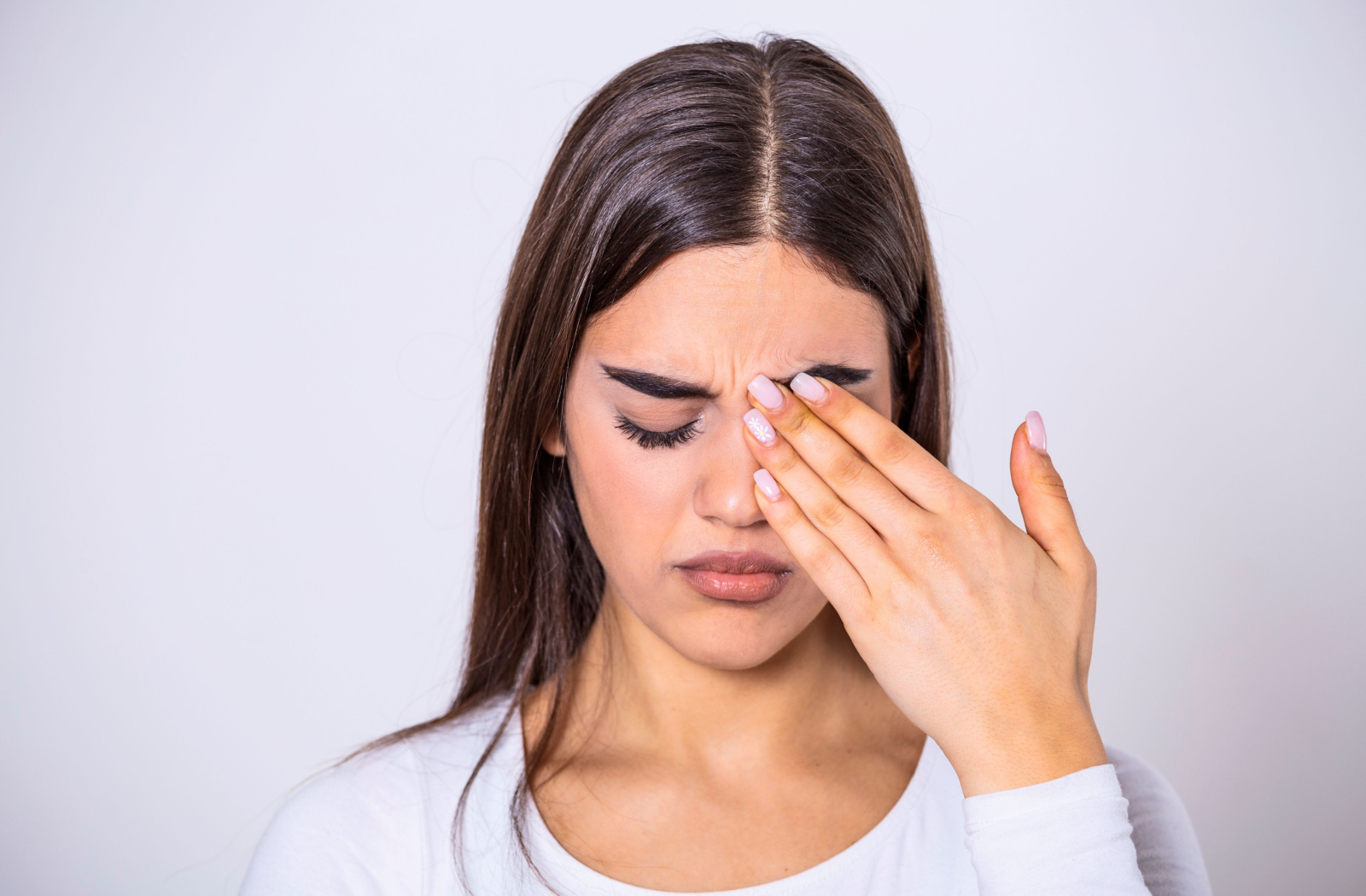 A woman with eyes closed rubbing her left eye with her left hand.