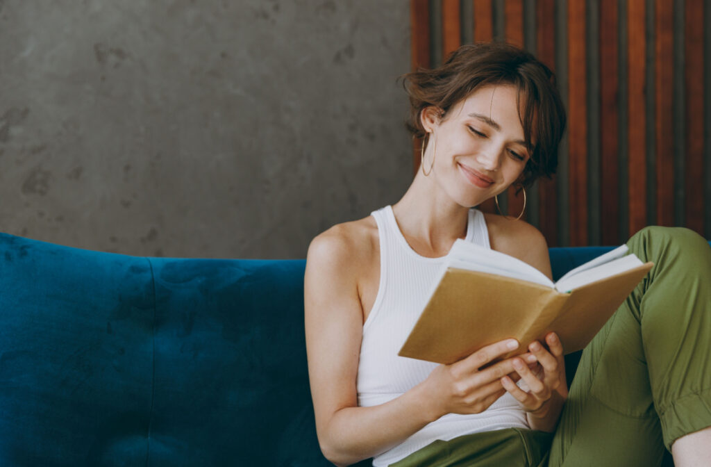 A woman happily reading a book while sitting on a couch.