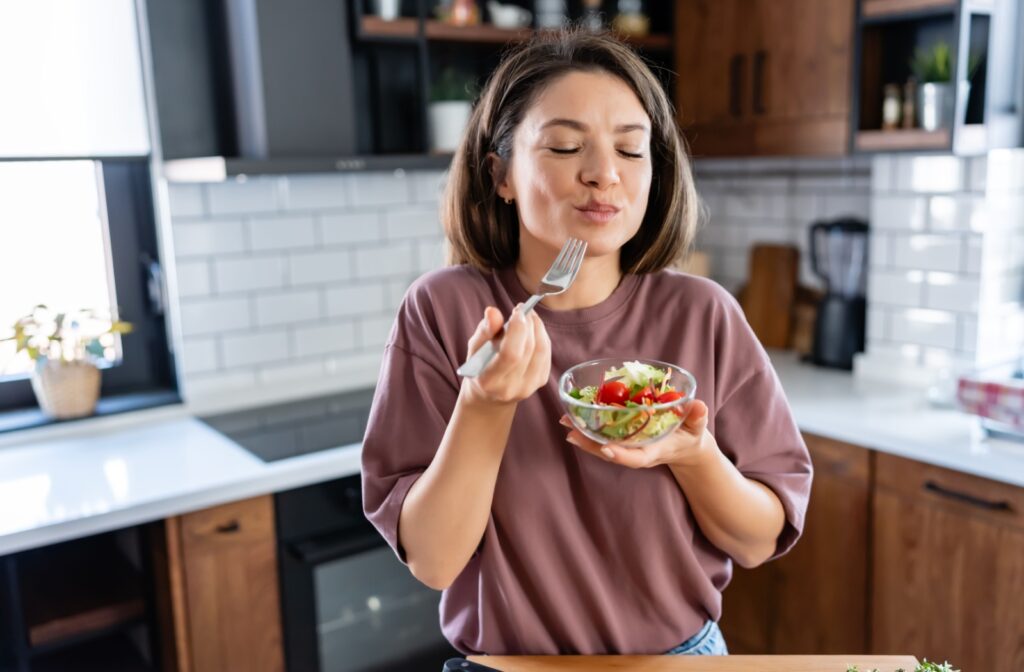 A woman in a cozy kitchen enjoying a fresh salad, smiling as she takes a bite.